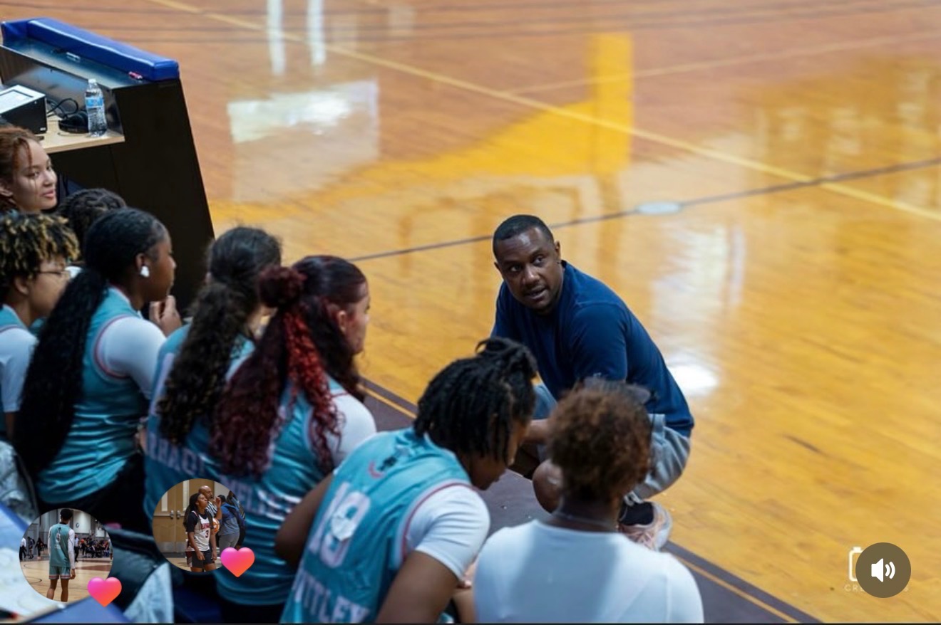 Coach crouched at the sideline giving instructions to seated players during a game.