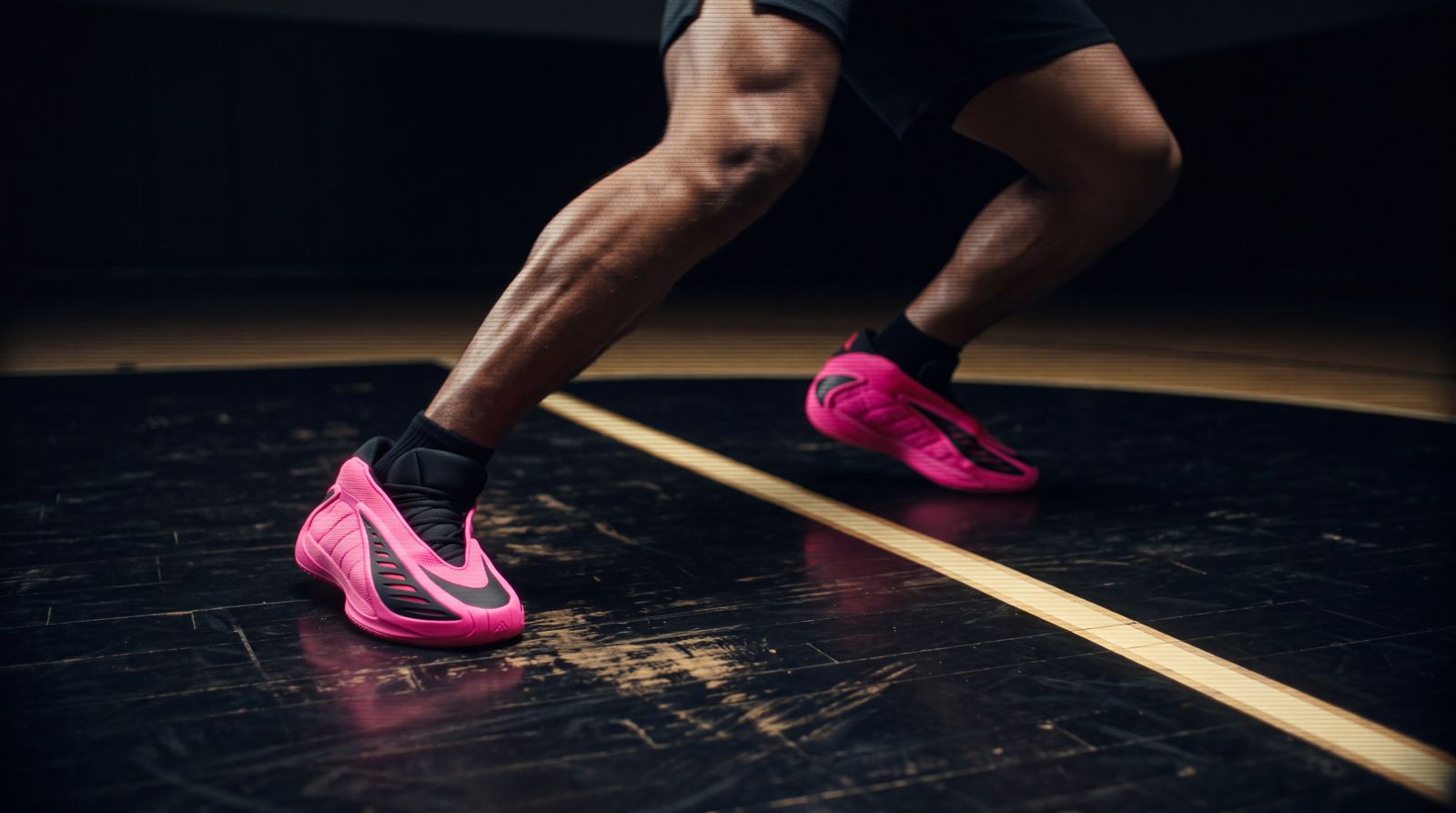 Athlete in a low defensive stance on a basketball court, showing footwork and bright pink shoes